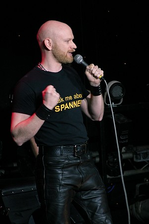 John on stage, wearing black leather and holding a microphone