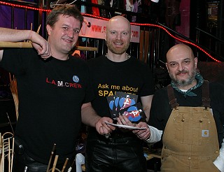 Master Cosmic, John and Derek stand in a line holding a cheque