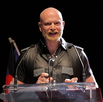 John at a lectern wearing a black leather shirt