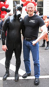 John on the gay pride parade next to someone in a full rubber outfit