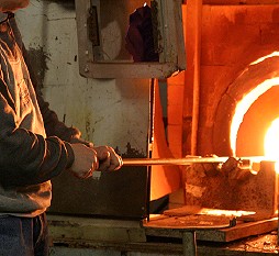 A close up of a vase being heated in a furnace, on the end of a long pole