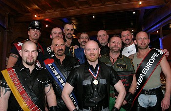 A group of leather titleholders, wearing sashes and medals, pose for the camera
