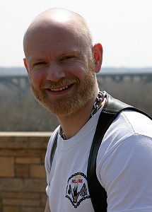 Headshot of John in a white t-shirt, smiling at the camera