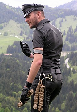 Dogtrainer wearing a black leather shirt and black leather jeans on top of a mountain