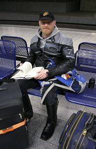 John on a cold hard metal seat surrounded by baggage waiting for a train in Belgium
