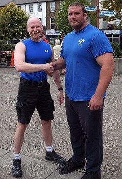 Full body shot of John shaking hands with Terry Hollands, both wearing bright blue t-shirts