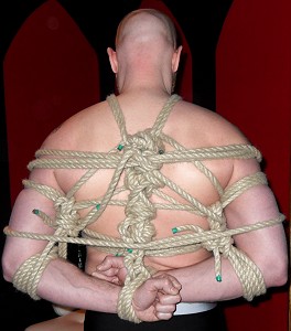 Close up of John from behind with his hands tied behind his back. Lots and lots of rope!
