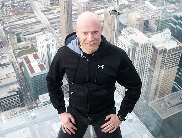 John sitting in a glass cube, looking up at the camera