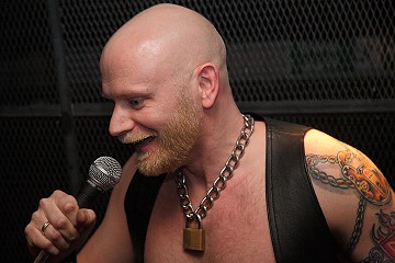 John wearing a leather vest, speaking into the microphone