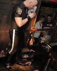 John standing in full leather interviewing Rex, in full rubber and on all fours, on stage at the Hoist.