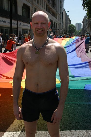 John in front of a giant rainbow flag at the start of the Europride parade in London