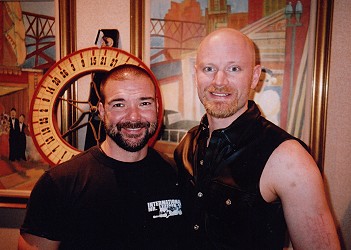 John standing next to Jason Hendrix. Behind Jason's head is a vertical roulette wheel used for fundraising